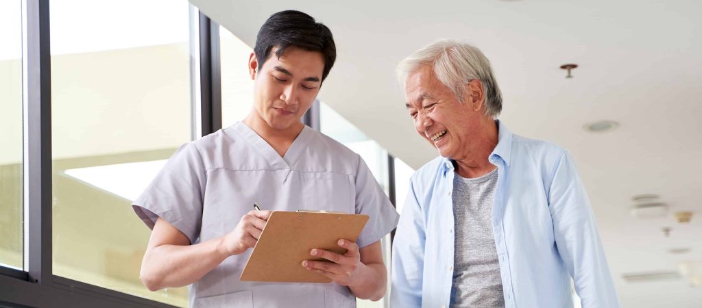 Young chiropractor talking to an older patient and taking notes.