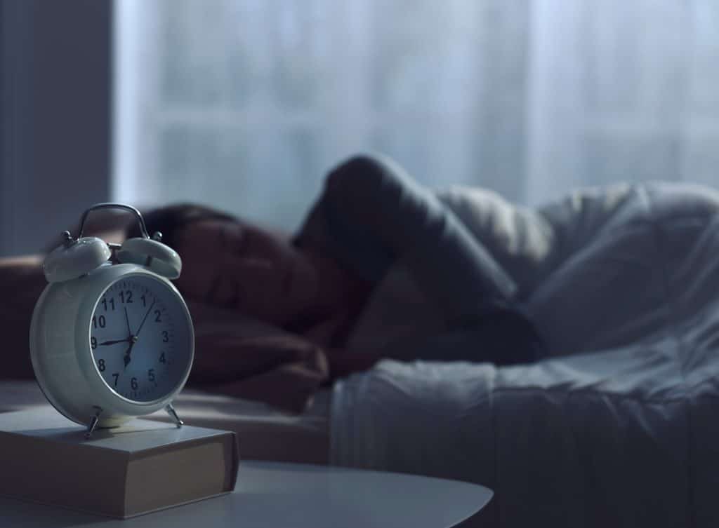 Serene woman sleeping in her bed and alarm clock in the foreground