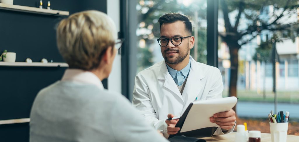 Smiling male doctor in consultation with a senior woman patient in a modern office.