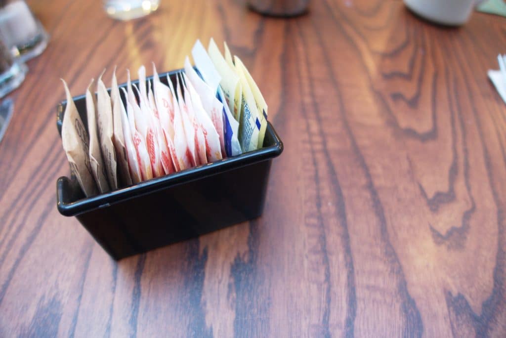 Closeup image of a table with a small black container holding different sugar packets.